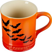 Orangefarbene Le-Creuset-Tasse mit schwarzem Fledermausmotiv und cremefarbener Innenseite, aus schräger Vorderansicht von oben