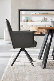 Moderner Armlehnstuhl in Seitenansicht, mit schwarzem Lederbezug und Metallbeinen, neben einem Holztisch.