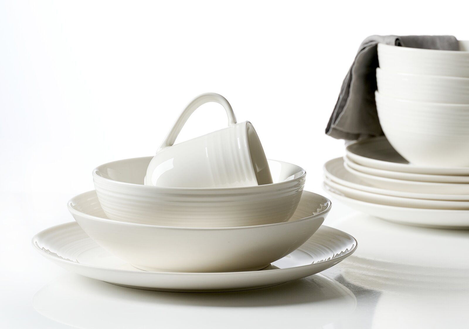 Elegantes weißes Geschirrset mit feiner Rillenstruktur, bestehend aus Tellern, Schalen und einer Tasse, aus leicht erhöhter frontaler Perspektive arrangiert