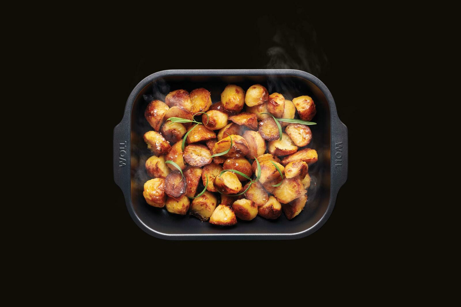 Vogelperspektive auf eine Bratreine mit goldbraun gebratenen Kartoffeln, garniert mit frischen Kräutern.