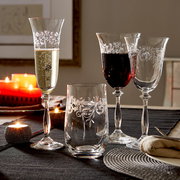 Vier elegante Weingläser mit filigranem Muster, gefüllt mit Weißwein und Rotwein, auf einem festlich gedeckten Tisch mit Kerzenlicht, seitliche Perspektive.