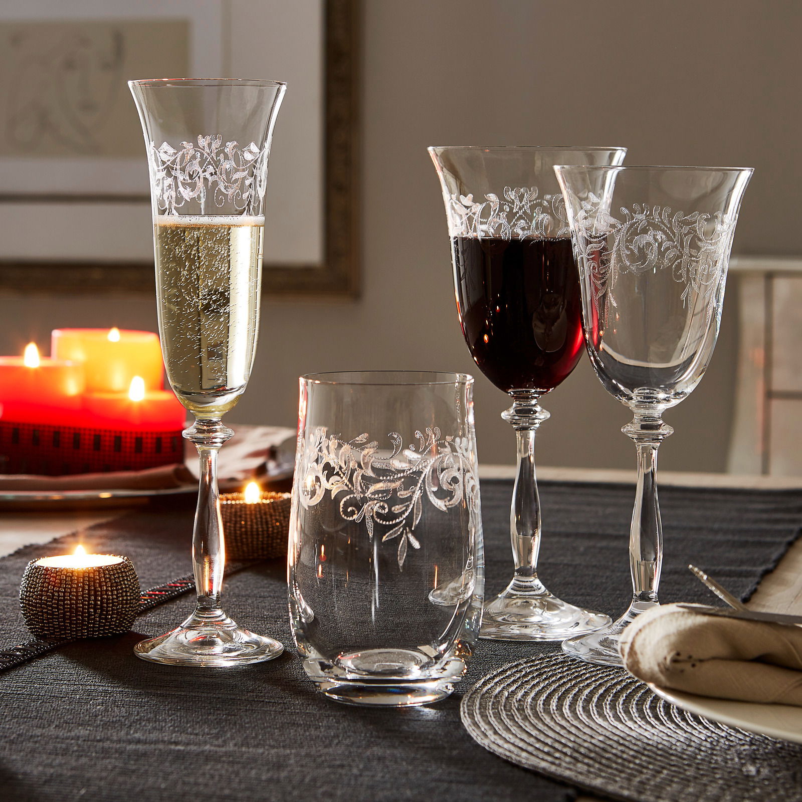 Vier elegante Weingläser mit filigranem Muster, gefüllt mit Weißwein und Rotwein, auf einem festlich gedeckten Tisch mit Kerzenlicht, seitliche Perspektive.