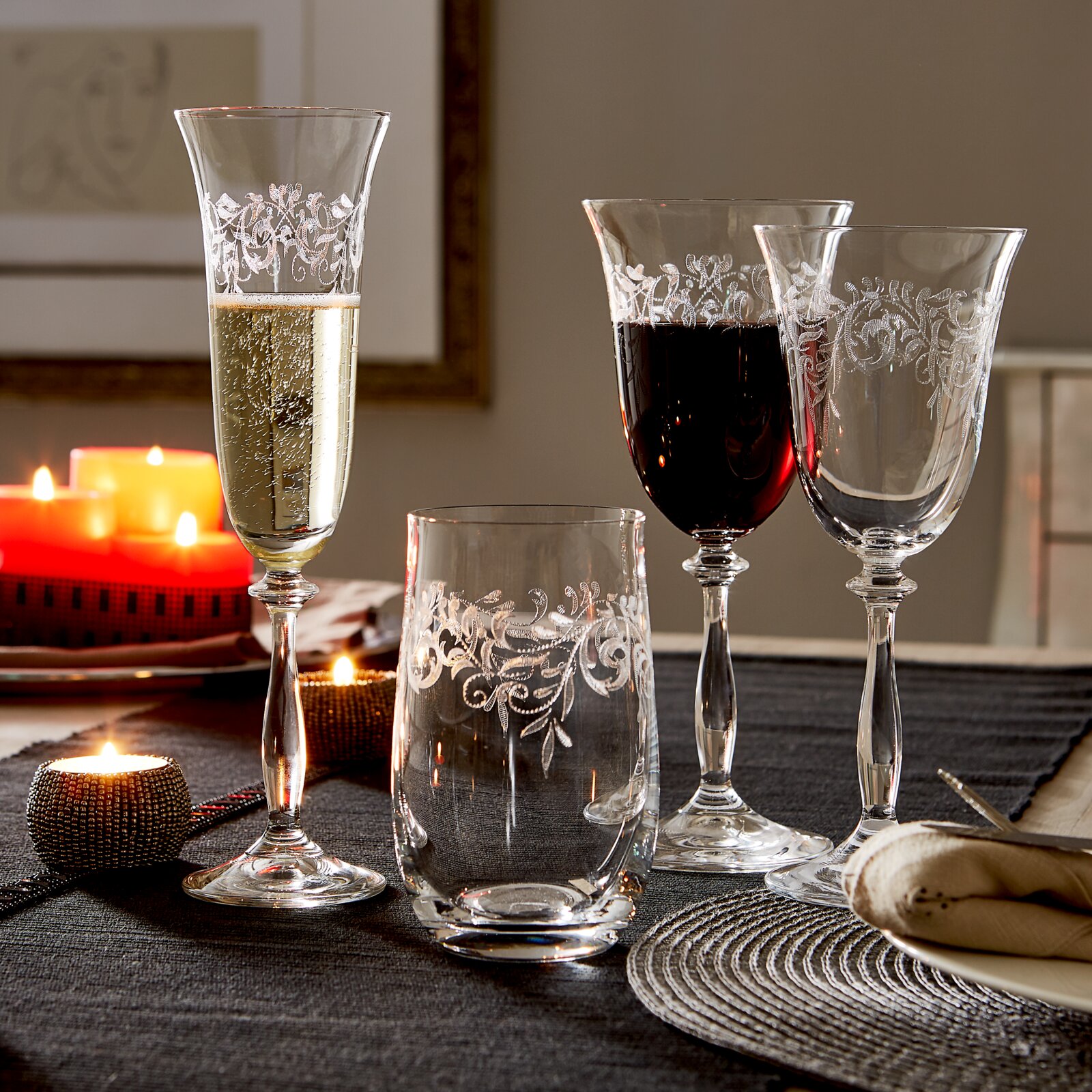 Vier elegante wijnglazen met een filigraanpatroon, gevuld met witte en rode wijn, op een feestelijk gedekte tafel bij kaarslicht, zijaanzicht.