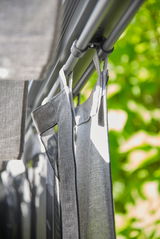 Nahaufnahme eines grauen Vorhangs, der an einer Stange hängt, mit einem Hintergrund aus grünen Blättern.