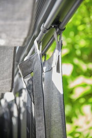 Nahaufnahme eines grauen Vorhangs, der an einer Stange hängt, mit einem Hintergrund aus grünen Blättern.