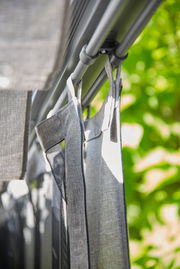 Nahaufnahme eines grauen Vorhangs, der an einer Stange hängt, mit einem Hintergrund aus grünen Blättern.