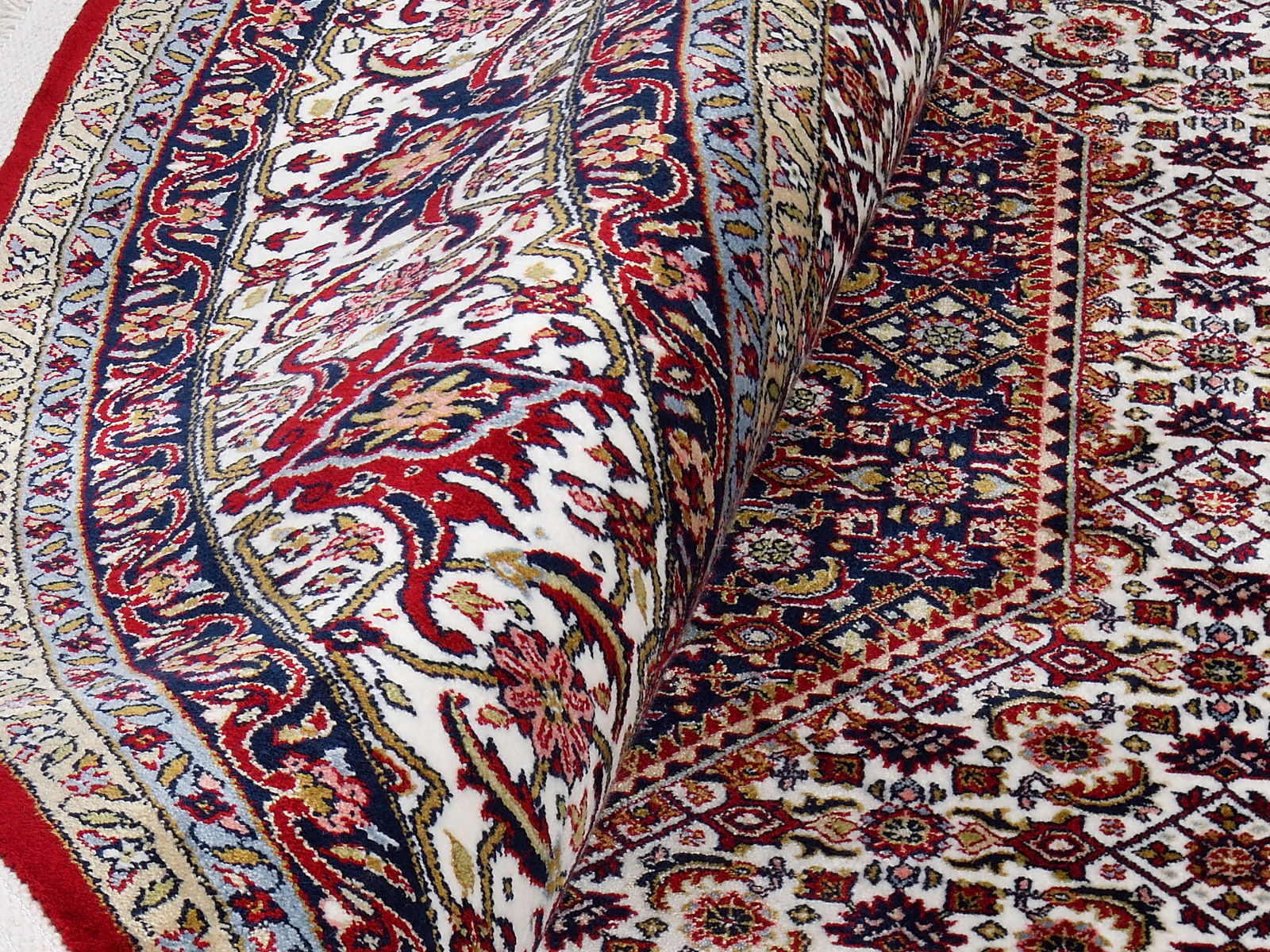 Nahaufnahme eines kunstvoll gemusterten Orientteppichs mit roten, blauen und beigen Details, teilweise aufgerollt.