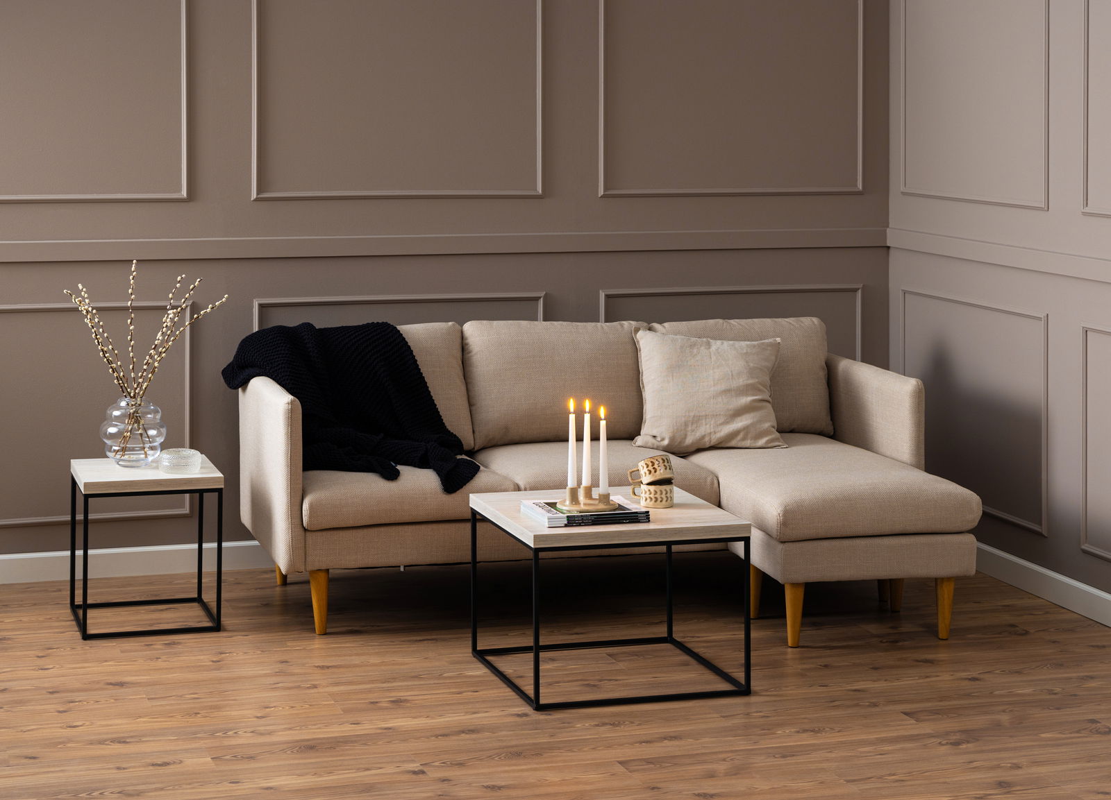 Moderner Couchtisch mit schwarzem Metallgestell und heller Holzplatte, frontal vor einem beigen Sofa in einem stilvoll eingerichteten Wohnzimmer.