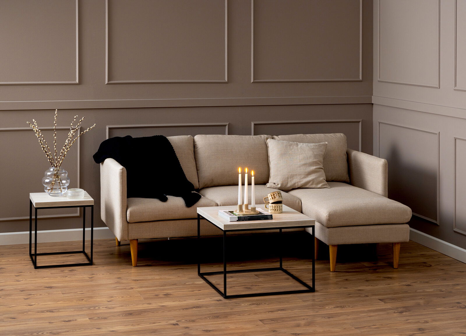 Moderner Couchtisch mit schwarzem Metallgestell und heller Holzplatte, frontal vor einem beigen Sofa in einem stilvoll eingerichteten Wohnzimmer.