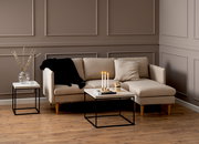 Moderner Couchtisch mit schwarzem Metallgestell und heller Holzplatte, frontal vor einem beigen Sofa in einem stilvoll eingerichteten Wohnzimmer.