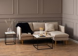 Moderner Couchtisch mit schwarzem Metallgestell und heller Holzplatte, frontal vor einem beigen Sofa in einem stilvoll eingerichteten Wohnzimmer.