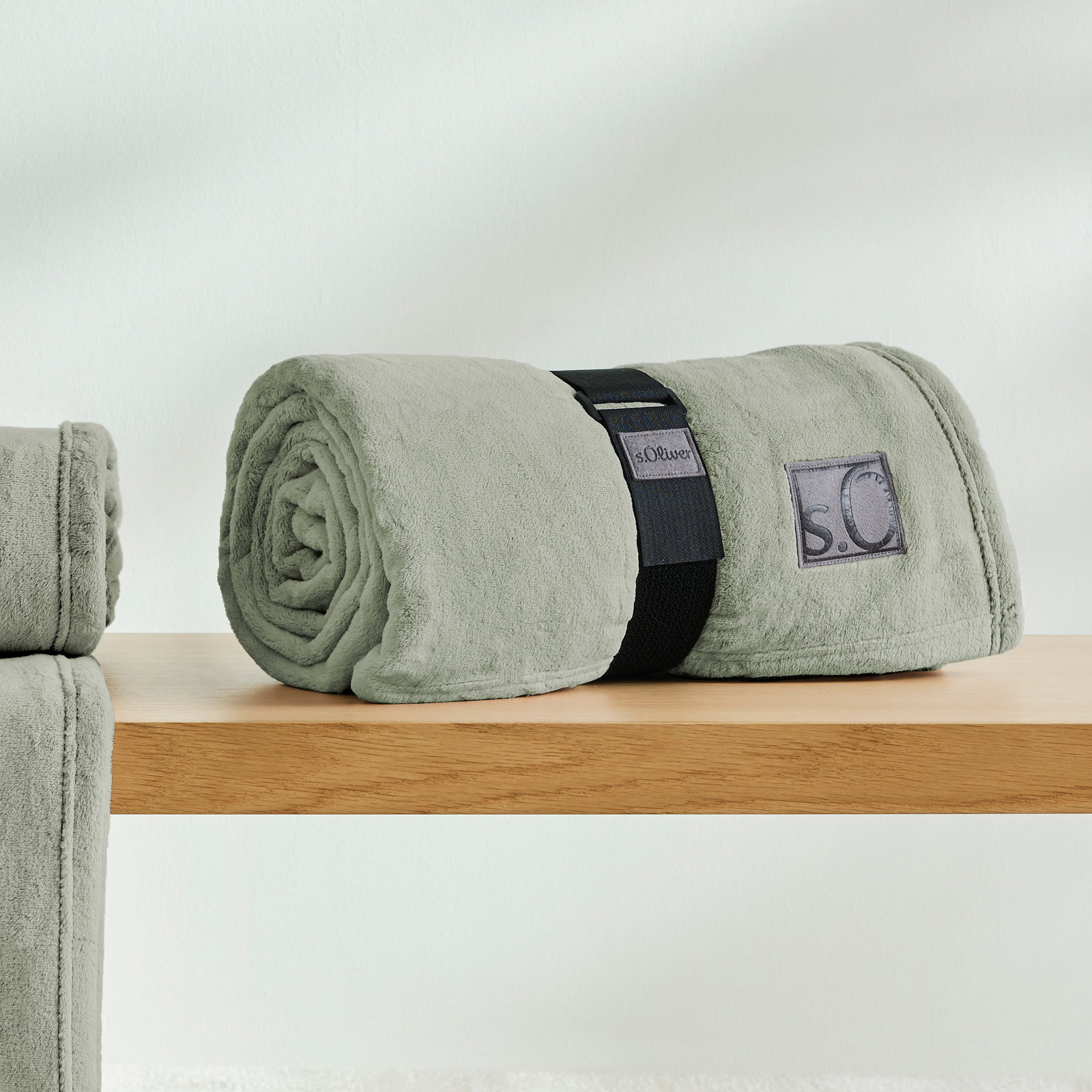 Graue, gerollte Kuscheldecke von s.Oliver auf einem Holztisch, seitliche Perspektive