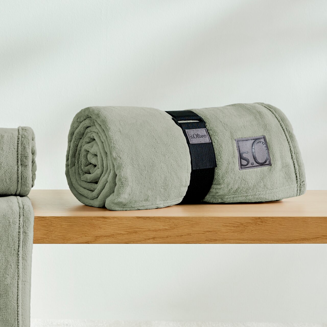Graue, gerollte Kuscheldecke von s.Oliver auf einem Holztisch, seitliche Perspektive