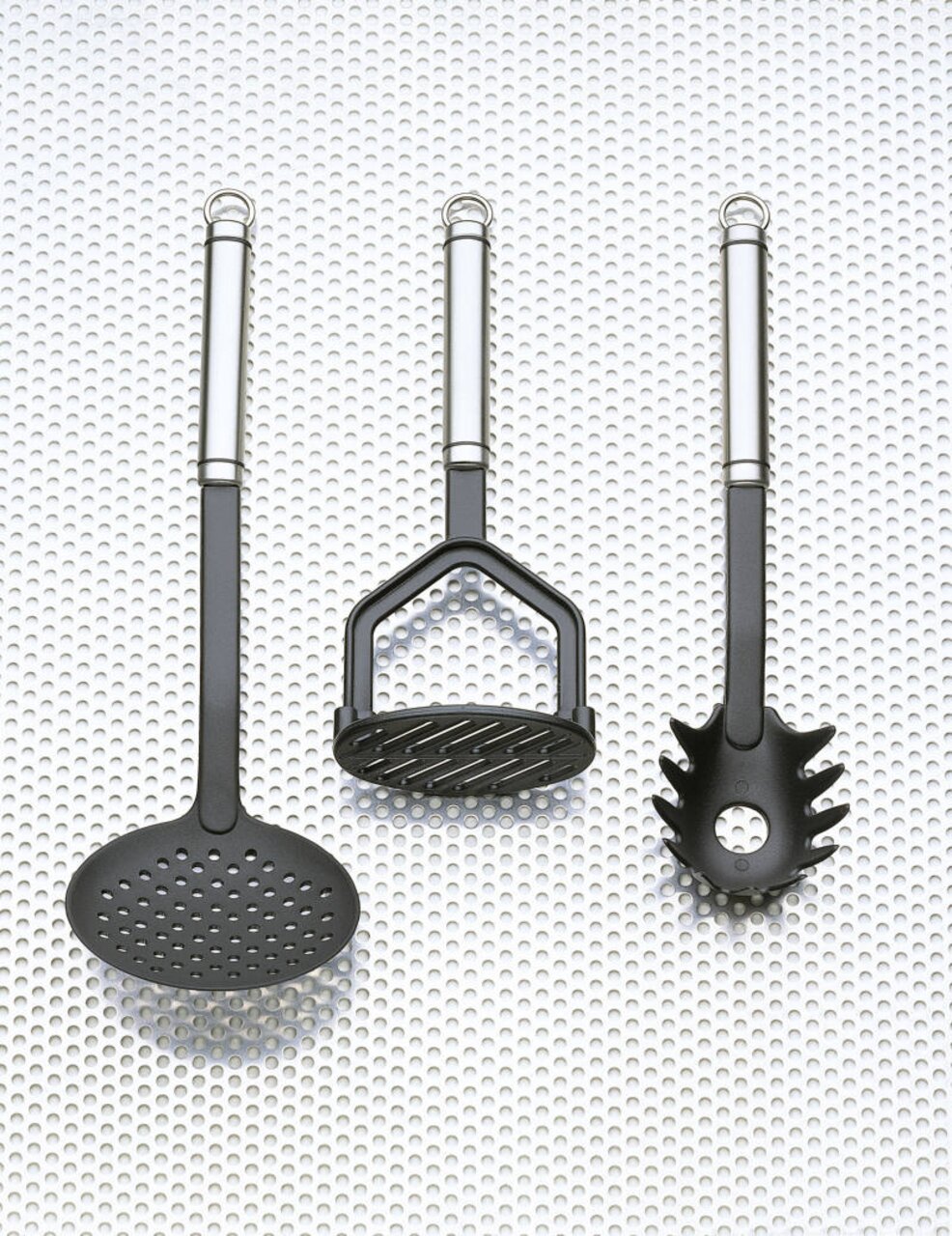 Drei Küchenutensilien aus der Vogelperspektive: ein Schaumlöffel, ein Kartoffelstampfer und ein Spaghettilöffel, alle mit Edelstahlgriffen.