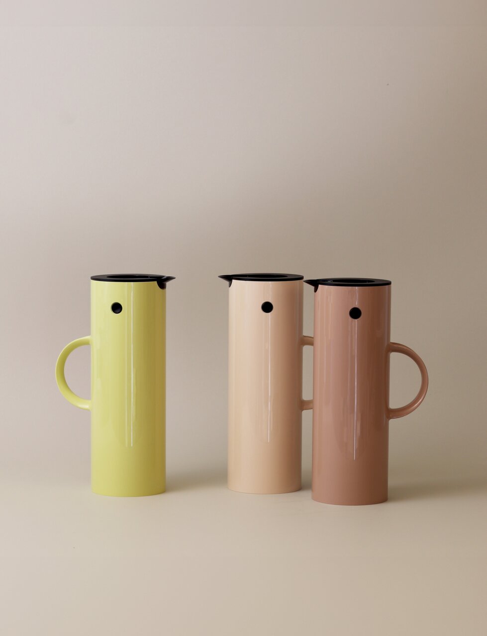 Drei EM77 Isolierkannen in verschiedenen Farben, von links nach rechts: hellgrün, beige und rosa, frontal fotografiert.
