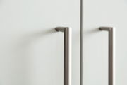 Nahaufnahme von zwei modernen, silbernen Griffen an einem weißen Schuhschrank, seitliche Perspektive