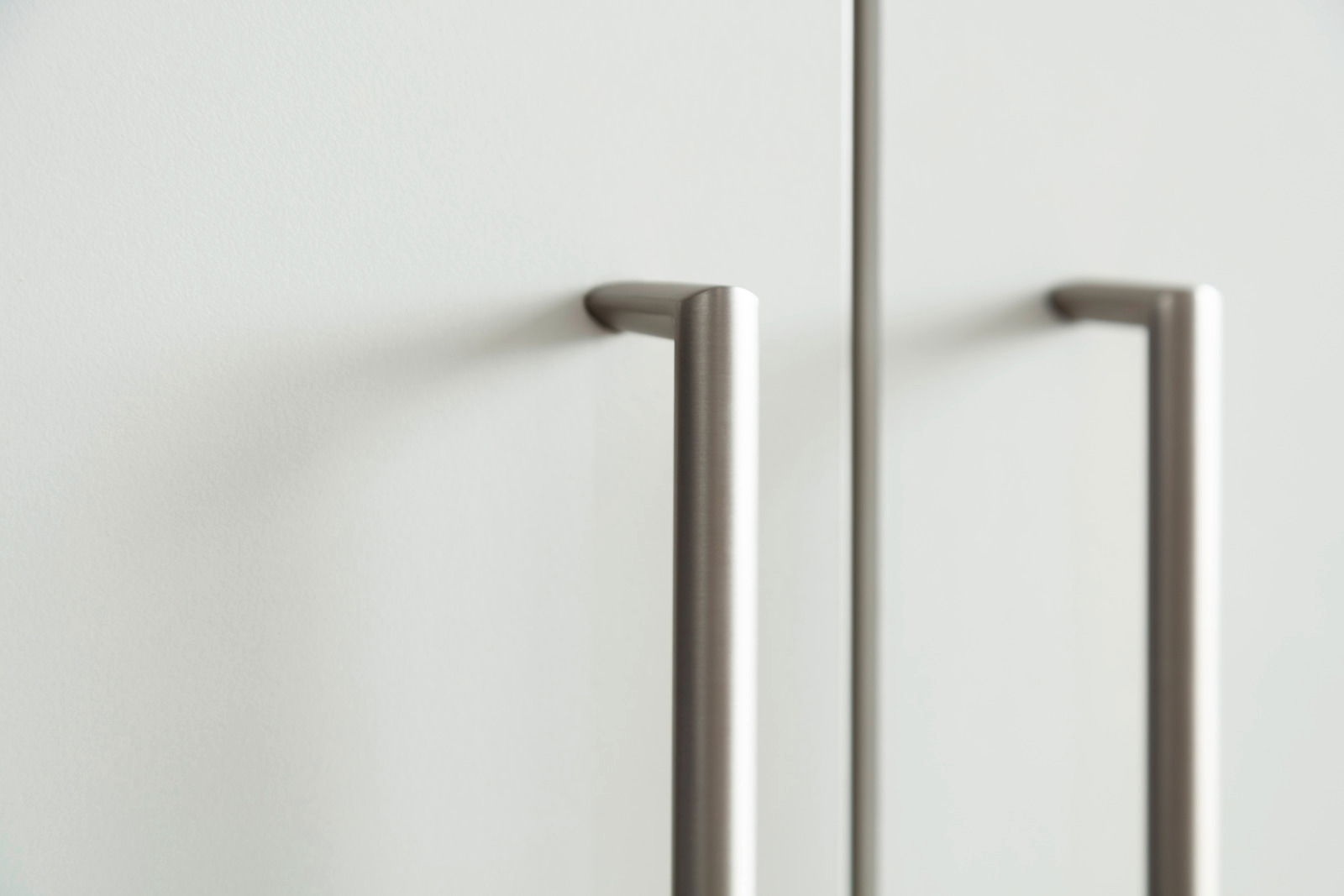 Nahaufnahme von zwei modernen, silbernen Griffen an einem weißen Schuhschrank, seitliche Perspektive