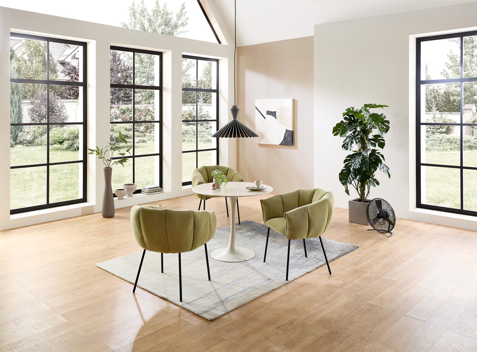 Z2 Esstisch rund JOSH Modernes Esszimmer-Set mit rundem weißem Tisch und vier olivgrünen Polsterstühlen auf Teppich in hellem Raum mit großen Fenstern, Perspektive: leicht erhöhte Frontansicht.