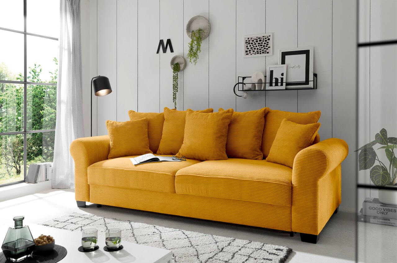 Hom´in Big Sofa MAUREEN Gelbes Funktionssofa mit mehreren Kissen in einem modernen Wohnzimmer, seitliche Perspektive.