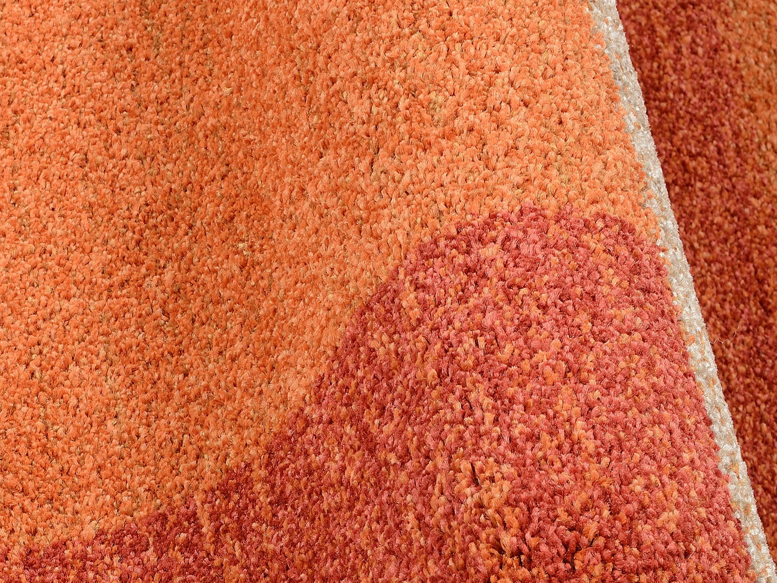 Nahaufnahme eines orange-roten Teppichs mit strukturierter Oberfläche, seitliche Perspektive