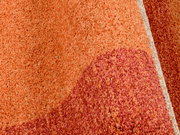 Nahaufnahme eines orange-roten Teppichs mit strukturierter Oberfläche, seitliche Perspektive