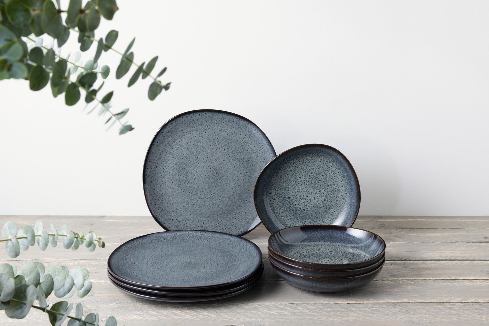 Like by Villeroy & Boch Tafelservice 8-tlg. LAVE GRIS Ein 8-teiliges Tafelservice in dunklem Blau mit gesprenkeltem Muster, bestehend aus flachen und tiefen Tellern, auf einem Holztisch arrangiert. Die Perspektive ist frontal.