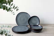Ein 8-teiliges Tafelservice in dunklem Blau mit gesprenkeltem Muster, bestehend aus flachen und tiefen Tellern, auf einem Holztisch arrangiert. Die Perspektive ist frontal.