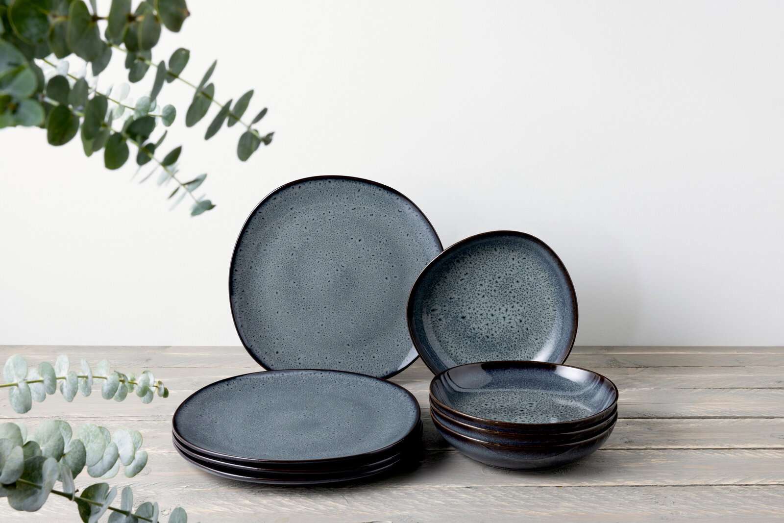 Ein 8-teiliges Tafelservice in dunklem Blau mit gesprenkeltem Muster, bestehend aus flachen und tiefen Tellern, auf einem Holztisch arrangiert. Die Perspektive ist frontal.