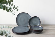 Ein 8-teiliges Tafelservice in dunklem Blau mit gesprenkeltem Muster, bestehend aus flachen und tiefen Tellern, auf einem Holztisch arrangiert. Die Perspektive ist frontal.