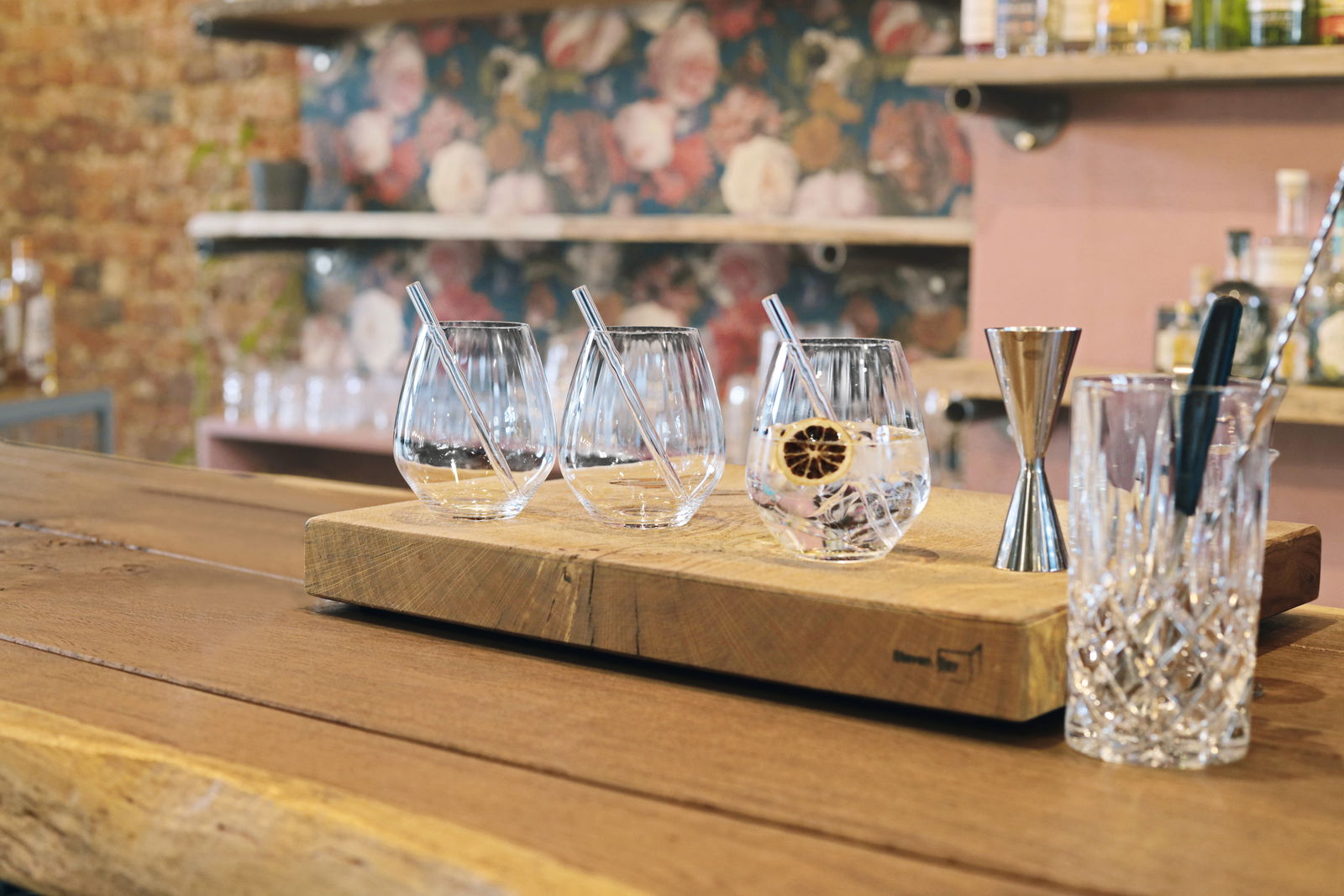 Drei Gin Tonic Gläser mit Glastrinkhalmen auf einem Holzbrett, seitliche Perspektive.