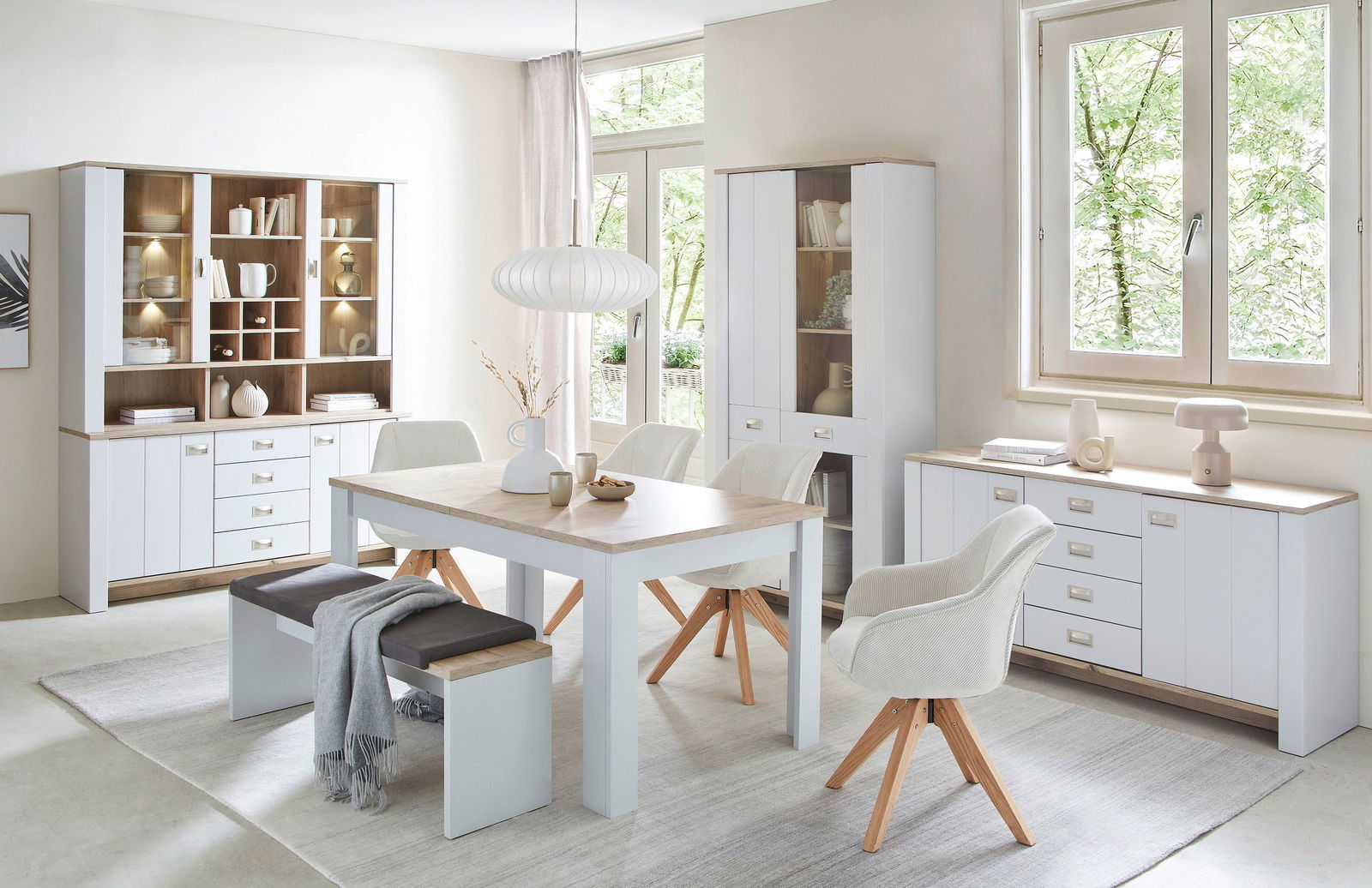 Esszimmer mit modernem Esstisch, Bank und Stühlen in heller Holzoptik, umgeben von Vitrinen und Sideboards, seitliche Perspektive