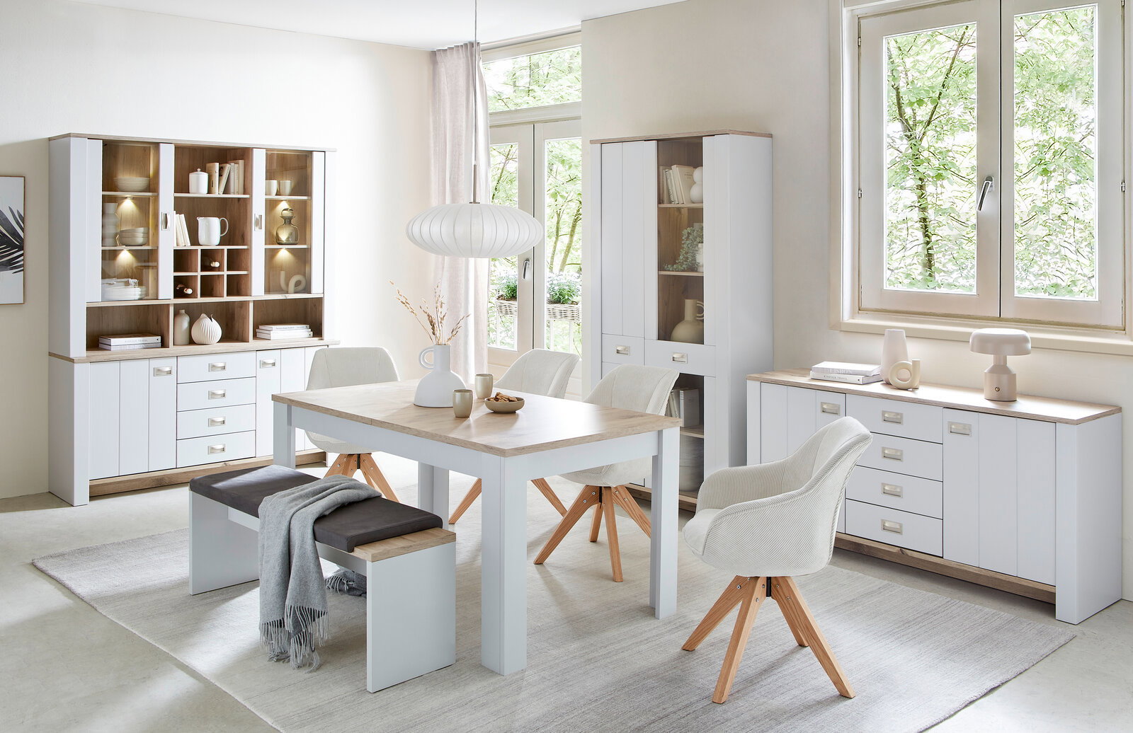 Esszimmer mit modernem Esstisch, Bank und Stühlen in heller Holzoptik, umgeben von Vitrinen und Sideboards, seitliche Perspektive