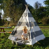 Kind spielt vor einem grau gestreiften Tipi-Zelt im Garten, seitliche Perspektive