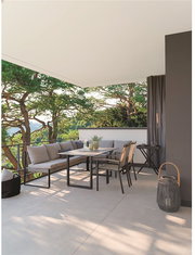 Moderne Outdoor-Lounge auf einer überdachten Terrasse mit grauem Ecksofa, Esstisch und Stühlen sowie Laterne, seitliche Perspektive