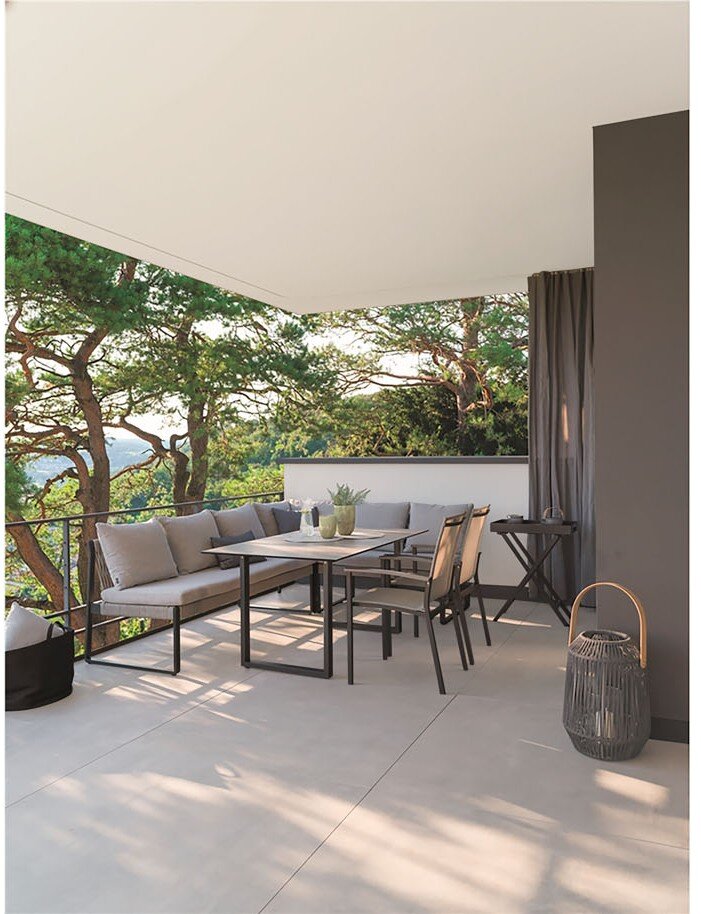 Moderne Outdoor-Lounge auf einer überdachten Terrasse mit grauem Ecksofa, Esstisch und Stühlen sowie Laterne, seitliche Perspektive