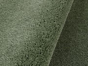 Nahaufnahme eines grünen, runden Teppichs mit weicher Textur, perspektivisch von oben fotografiert.