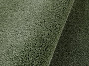 Nahaufnahme eines grünen, runden Teppichs mit weicher Textur, perspektivisch von oben fotografiert.