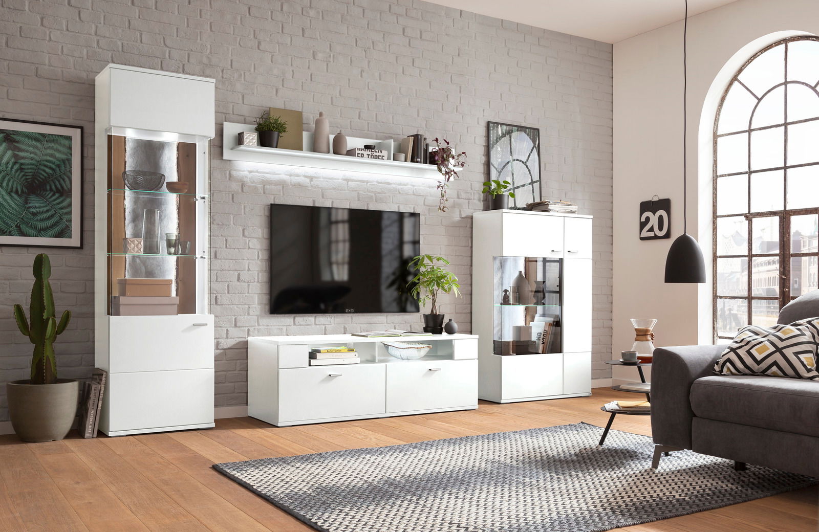 Set one by Musterring Wandboard TACOMA Modernes Wohnzimmer mit weißem Wandboard über einem Fernseher, umgeben von stilvollen Möbeln und Dekorationen, seitliche Perspektive.