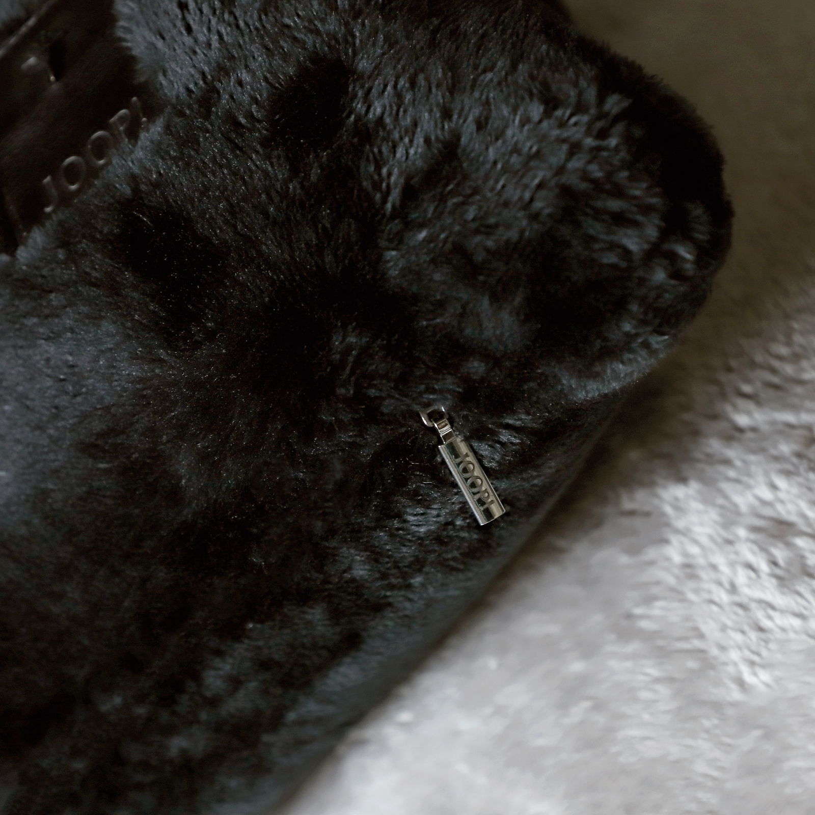 Nahaufnahme einer schwarzen, flauschigen Kissenhülle von JOOP! mit sichtbarem Reißverschlussanhänger. Perspektive von oben.