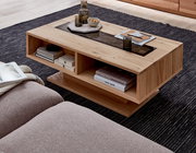 Moderner Couchtisch aus hellem Massivholz mit dunkler Glas- oder Stein-Einlage und offenen Ablagefächern, dekoriert mit Tablett, Gläsern und Büchern, in schräger Draufsicht im Wohnzimmer auf Teppich.