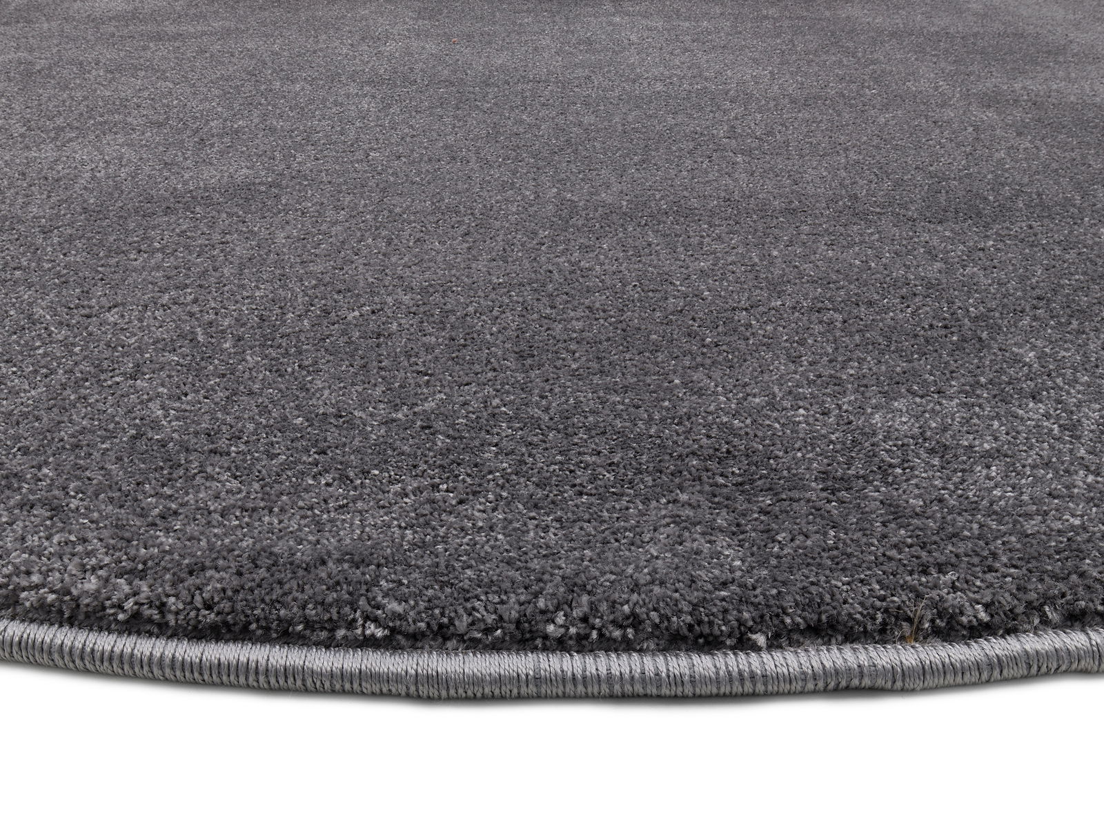 Grauer Uni-Teppich in Nahaufnahme, zeigt die Textur und den Rand des Teppichs aus seitlicher Perspektive.