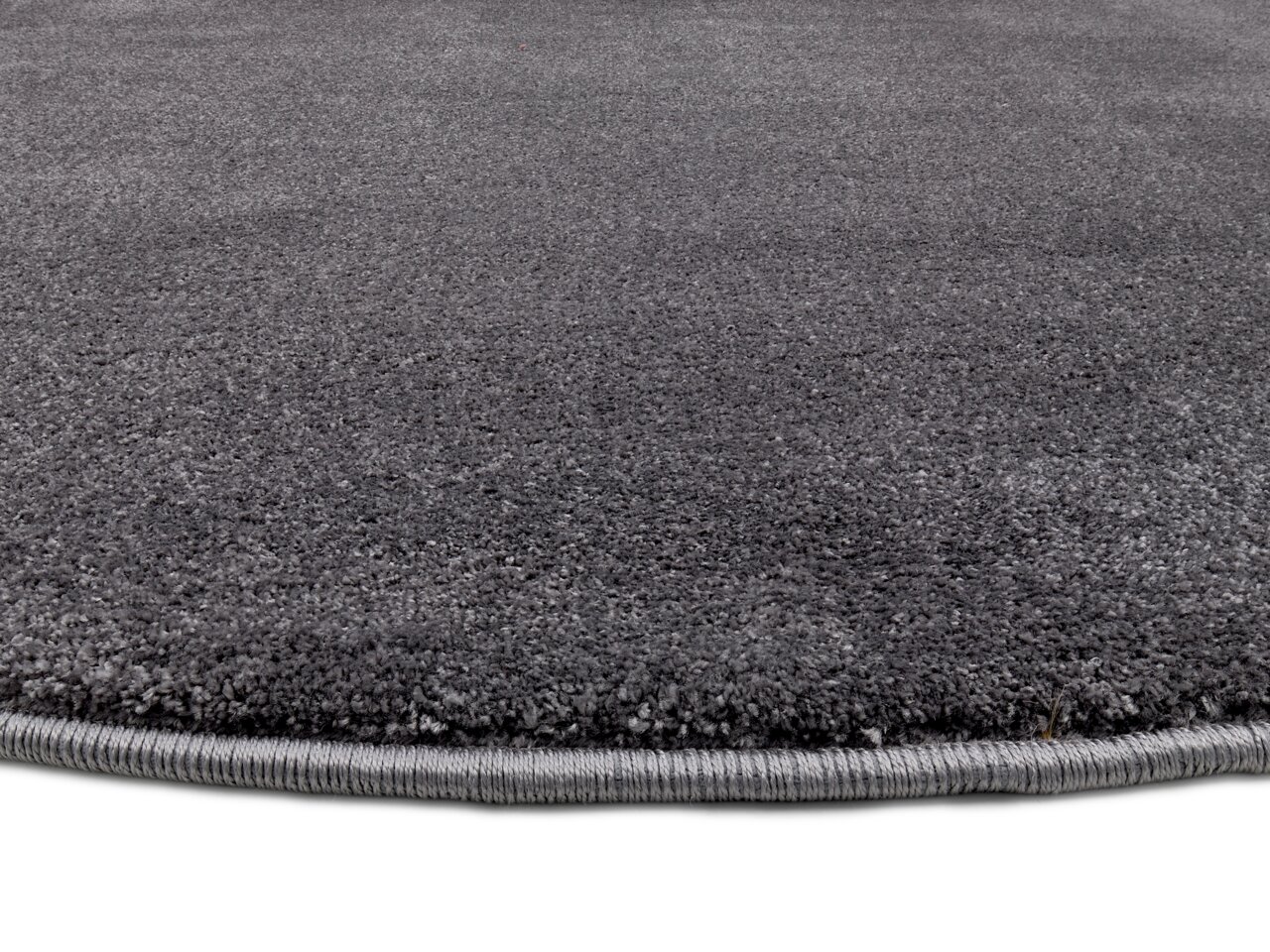 Grauer Uni-Teppich in Nahaufnahme, zeigt die Textur und den Rand des Teppichs aus seitlicher Perspektive.