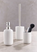 Dreiteiliges Badset in Weiß, bestehend aus einem Seifenspender, einer Toilettenbürste und einem Becher mit Make-up-Pinsel, aus seitlicher Perspektive fotografiert.