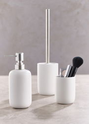 Dreiteiliges Badset in Weiß, bestehend aus einem Seifenspender, einer Toilettenbürste und einem Becher mit Make-up-Pinsel, aus seitlicher Perspektive fotografiert.