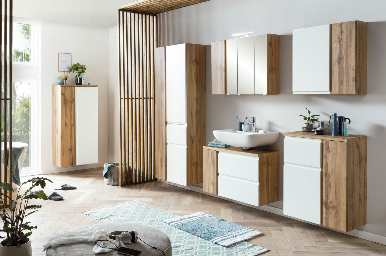 Moderner Waschbeckenunterschrank in Holzoptik mit weißer Front, rechts im Badezimmer platziert, aus seitlicher Perspektive fotografiert.