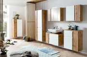 Moderner Waschbeckenunterschrank in Holzoptik mit weißer Front, rechts im Badezimmer platziert, aus seitlicher Perspektive fotografiert.