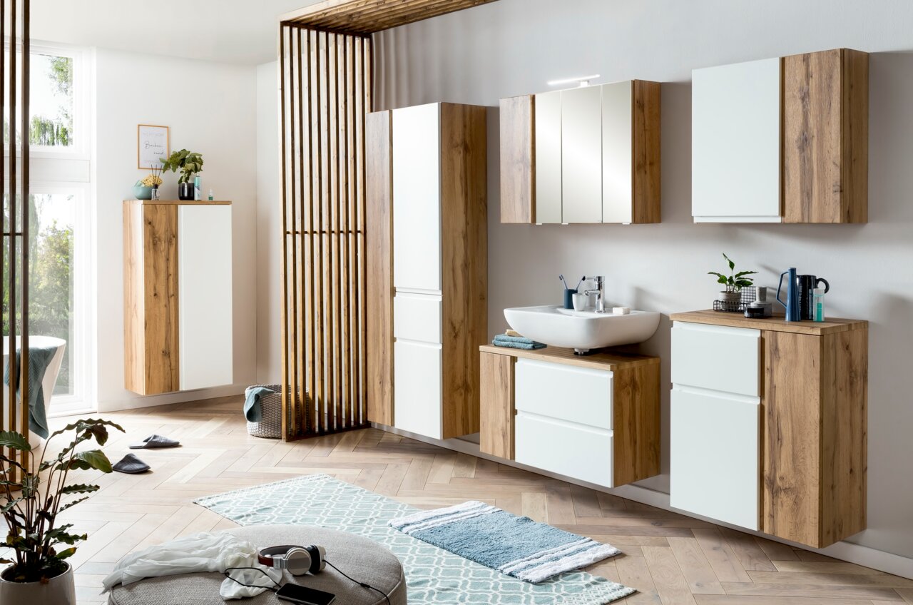 Moderner Waschbeckenunterschrank in Holzoptik mit weißer Front, rechts im Badezimmer platziert, aus seitlicher Perspektive fotografiert.