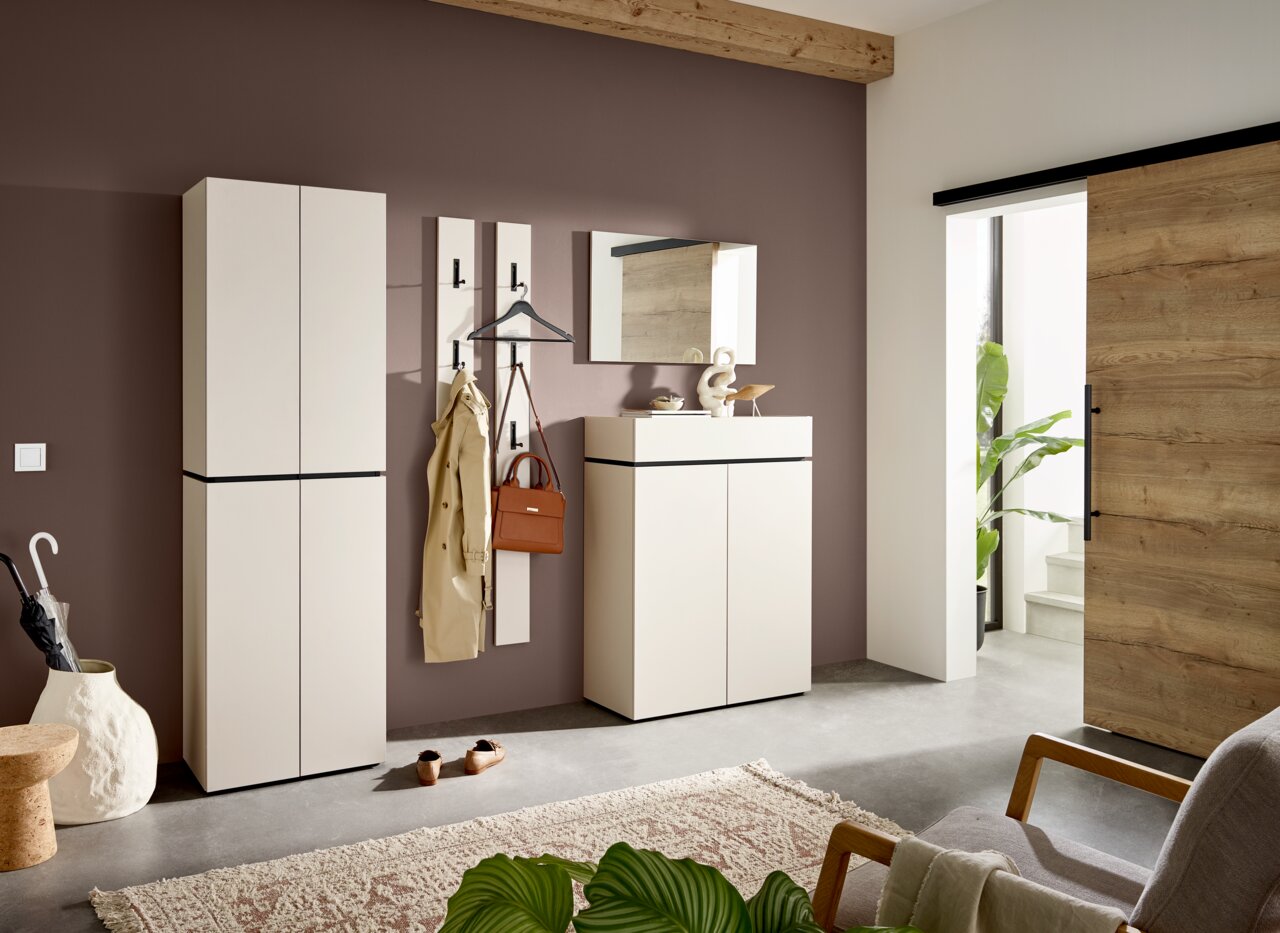 Moderner Eingangsbereich mit Garderobenmöbeln in heller Farbe, bestehend aus Schuhschrank, Garderobenpaneel und Spiegel, seitliche Perspektive.