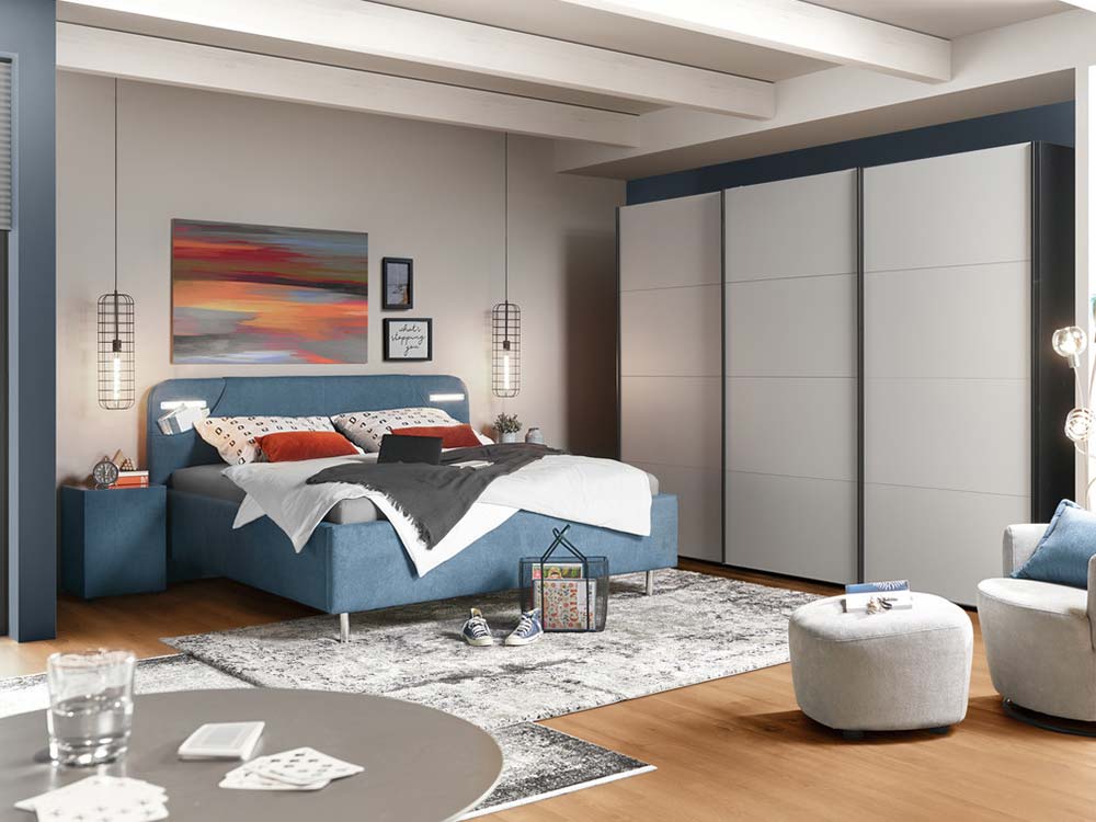 Helles Schlafzimmer mit blauem Bett und großem Schiebetürenschrank.