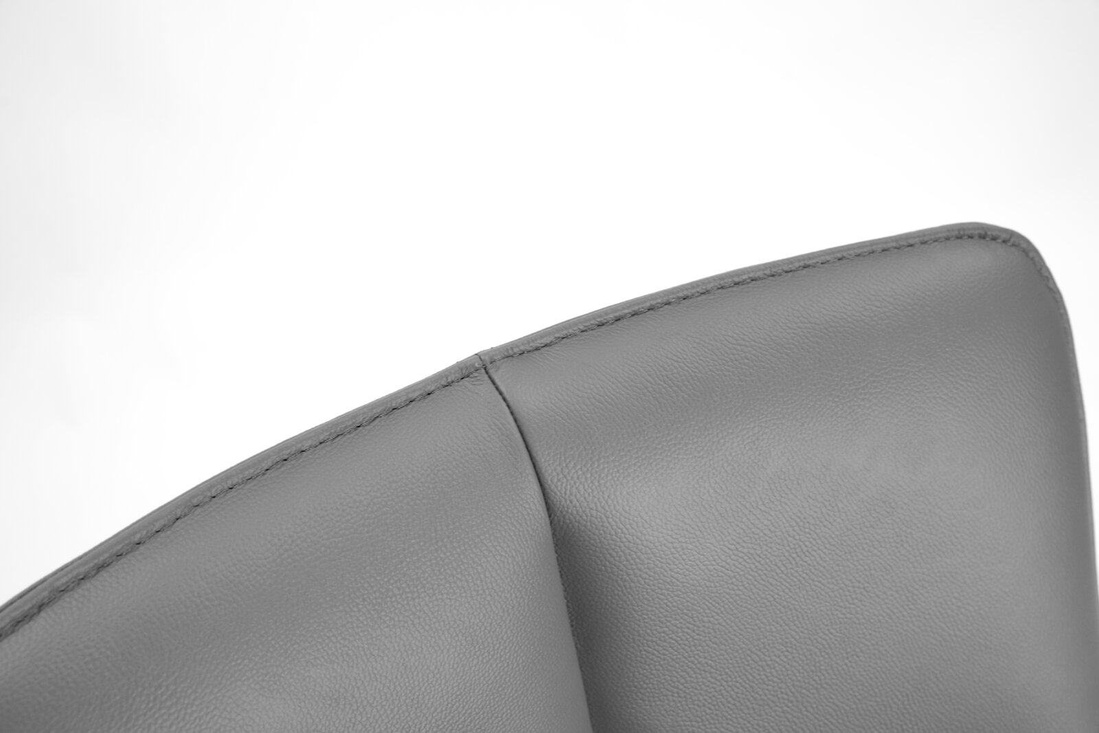 Close-up van de bovenhoek van een grijze leren fauteuil, gezien van bovenaf.
